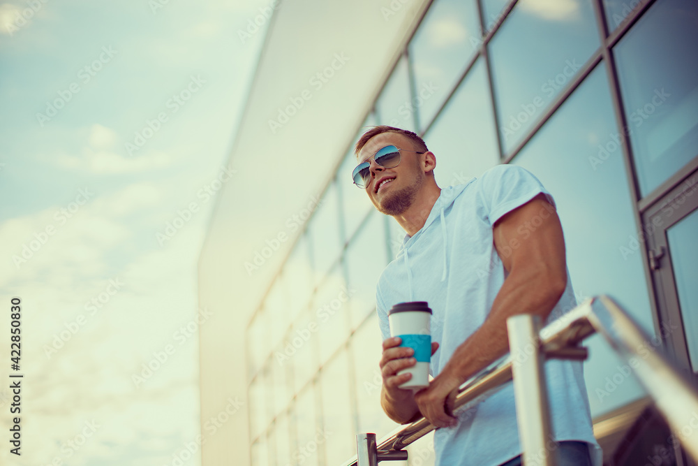 Young handsome man near city mall with cup of coffee looking up smiling and dreaming of something
