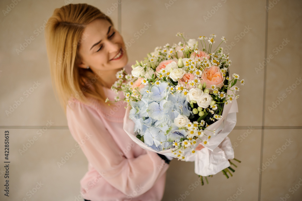 blonde woman holds bouquet of roses and hydrangeas and small daisies and looks at it blonde woman holds bouquet of roses and hydrangeas and small daisies and looks at it