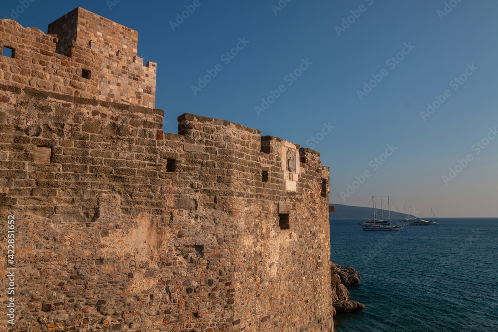 View of part of the old St. Peter's Castle in Bodrum, Turkey, the open blue sea and anchored sailboats. Ancient sights and modern holidays in Turkish resorts.
