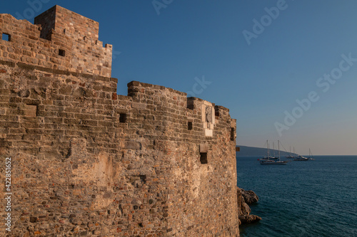 View of part of the old St. Peter's Castle in Bodrum, Turkey, the open blue sea and anchored sailboats. Ancient sights and modern holidays in Turkish resorts.