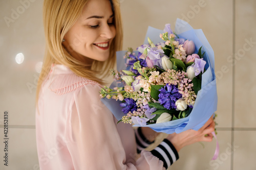 happy blonde woman holds floral bouquet of different fresh spring flowers in her hands