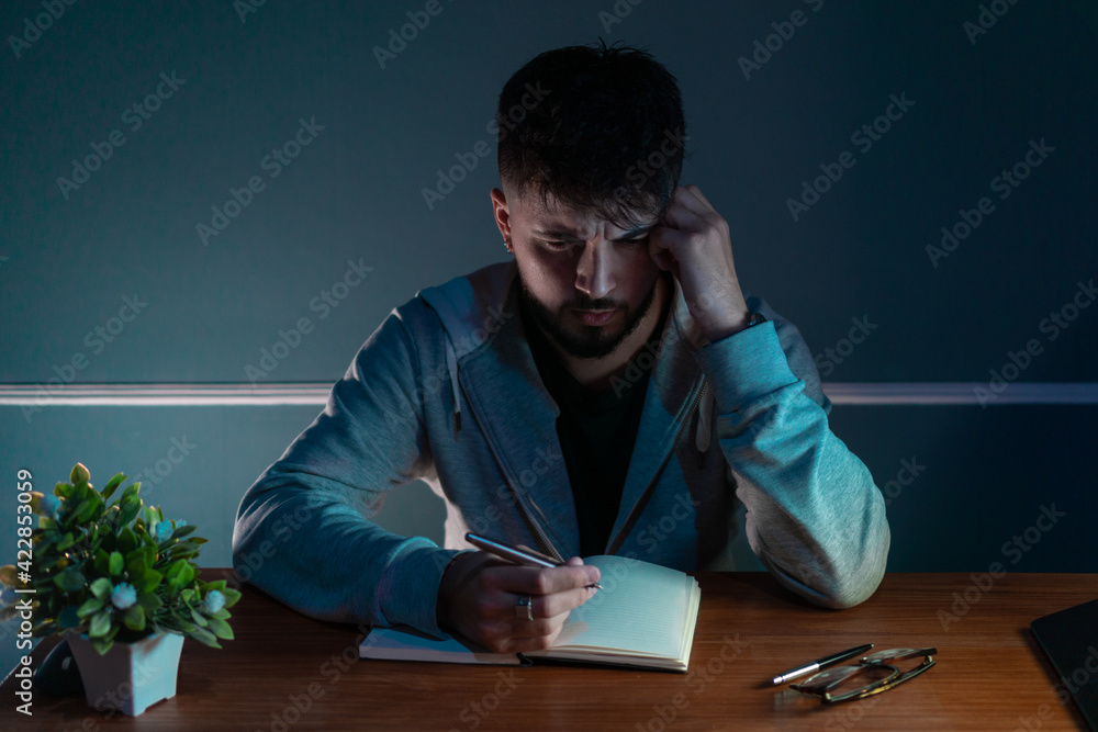 Obraz premium Young concentrated man writing a book in low light environment