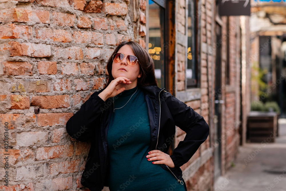 Portrait of stylish young pretty hipster woman in sunglasses and green dress, vintage urban background, street photo brick wall, looking away, Happy beautiful girl, body positivity, casual clothes