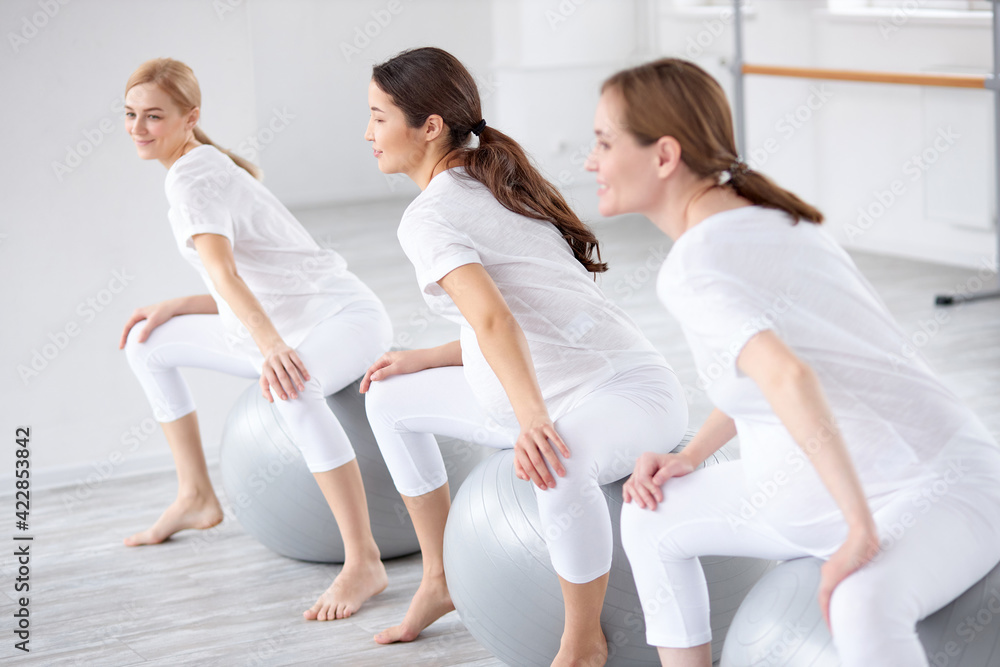 beautiful women in white sportswear training on fitballs doing exercises beautiful women in white sportswear training on fitballs doing exercises