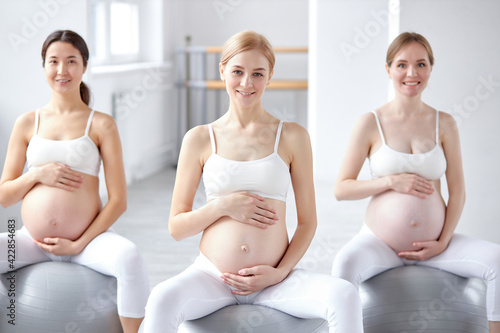 good-looking diverse pregnant women with naked tummy sit on fitballs engaged in perinatal gymnastics