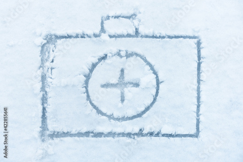 First aid kits suitcase sign is drawn on the white snow. Medical and pharmacy cross. Emergency health curing and safety concept.