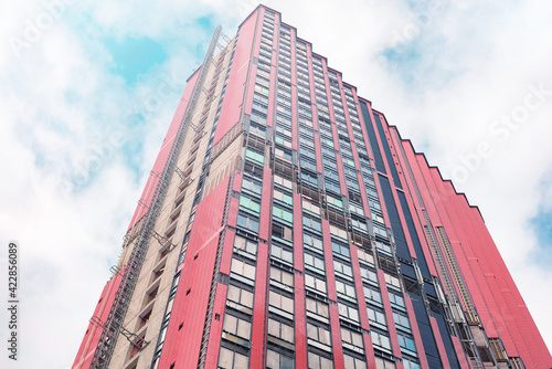 The facade of a red residential skyscraper under construction against the sky.