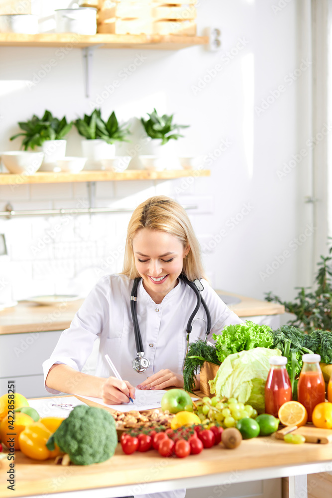 happy woman nutritionist standing near table full of healthy products in office