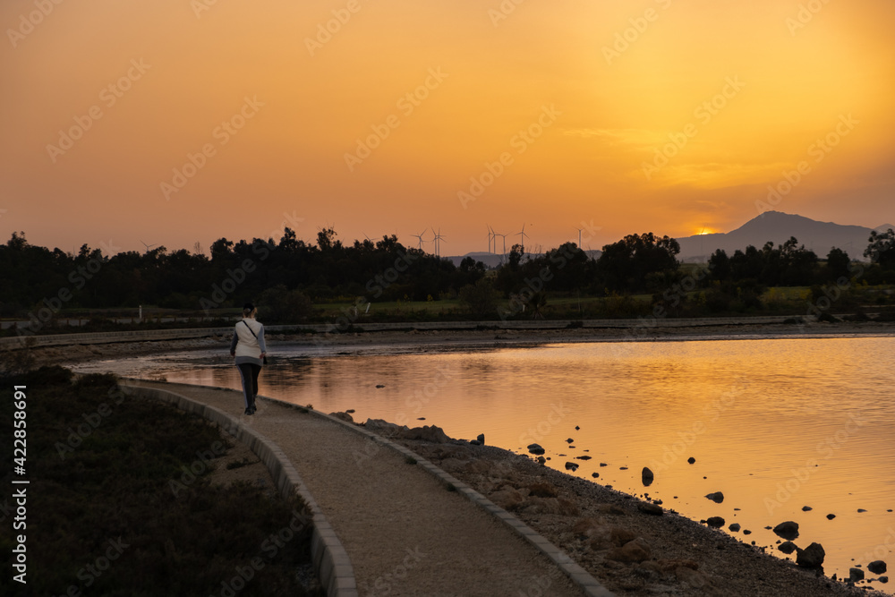 A woman walks at sunset along a footpath on Larnaca salt lake shore in Cyprus A woman walks at sunset along a footpath on Larnaca salt lake shore in Cyprus
