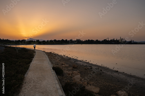 A woman walks at sunset along a footpath on Larnaca salt lake shore with the Hala Sultan Tekke mosque in the background © Iordanis Pallikaras