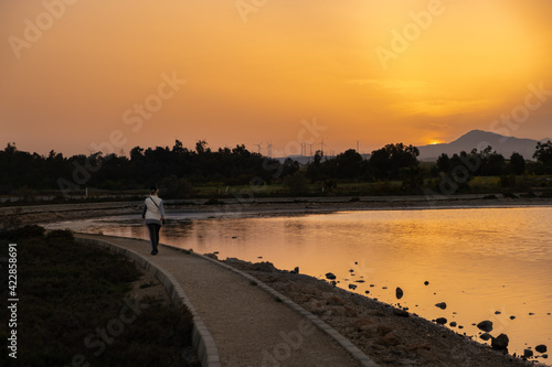 A woman walks at sunset along a footpath on Larnaca salt lake shore in Cyprus