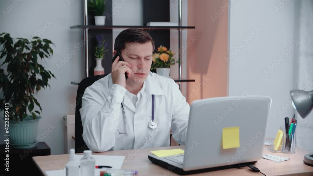 Male doctor sitting in the office in his office talking on the phone. Male doctor sitting in the office in his office talking on the phone.