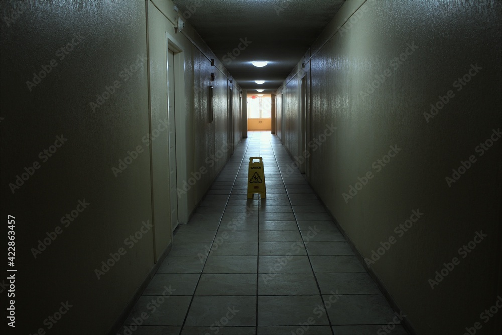 Creepy and scary looking hallway in an abandoned apartment building. A caution wet floor sign is placed on the floor. Also a concept for light at the end of the tunnel. 