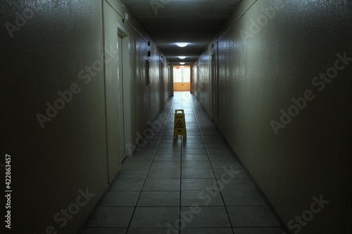 Creepy and scary looking hallway in an abandoned apartment building. A caution wet floor sign is placed on the floor. Also a concept for light at the end of the tunnel.  © Blue
