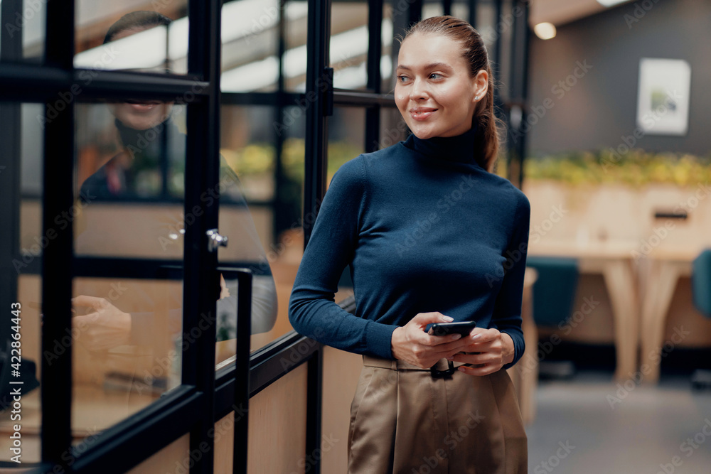 Fototapeta premium Portrait of a confident young woman French appearance brown hair. Holds a phone with documents and reports on a new project. Office clothes, favorite coworking job.