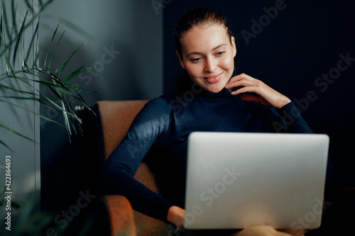 Beautiful European appearance brown-haired. Office clothes, favorite work. Portrait of a confident young woman working on a laptop computer in the office. Blue eyes, looking away.