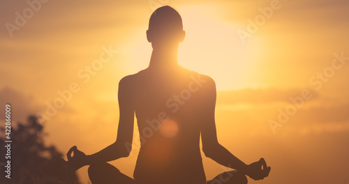Female silhouette meditating at sunset in a calm relaxed state of mind. 