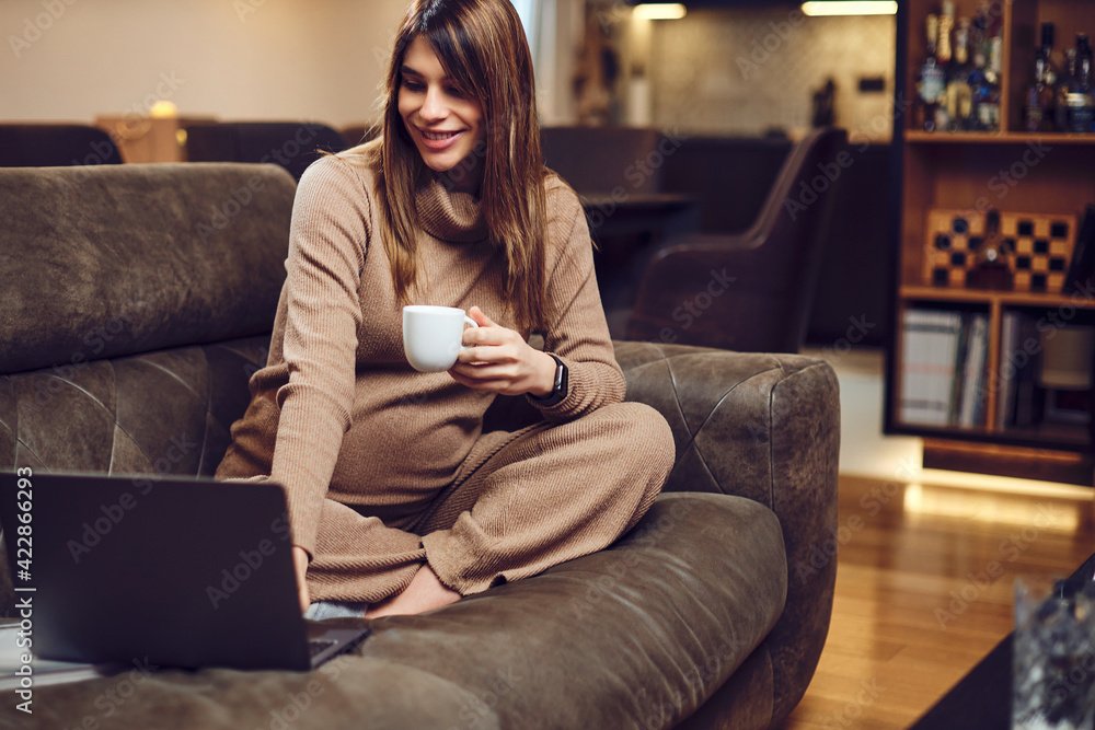 Smiling beautiful pregnant brunette sitting at her home, drinking tea and using laptop. Selective focus on hands. Blurred face Smiling beautiful pregnant brunette sitting at her home, drinking tea and using laptop. Selective focus on hands. Blurred face
