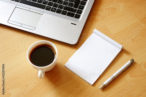 Laptop with coffee cup  notebook and pen on wooden background  concept for home office. Business concept. Work from home. desk office with laptop  blank notepad  coffee cup and pen on wooden table.
