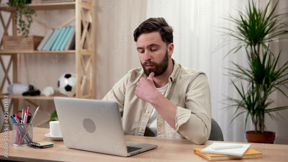 A man using a laptop sitting at a table in a home office. The man is typing on a laptop and thinking about something, resting his hand on his chin. Close up. Slow motion ready 59.97fps. A man using a laptop sitting at a table in a home office. The man is typing on a laptop and thinking about something, resting his hand on his chin. Close up. Slow motion ready 59.97fps.