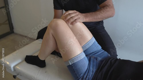 Anonymous physiotherapist checking ankles of female patient with bent knees on stretcher