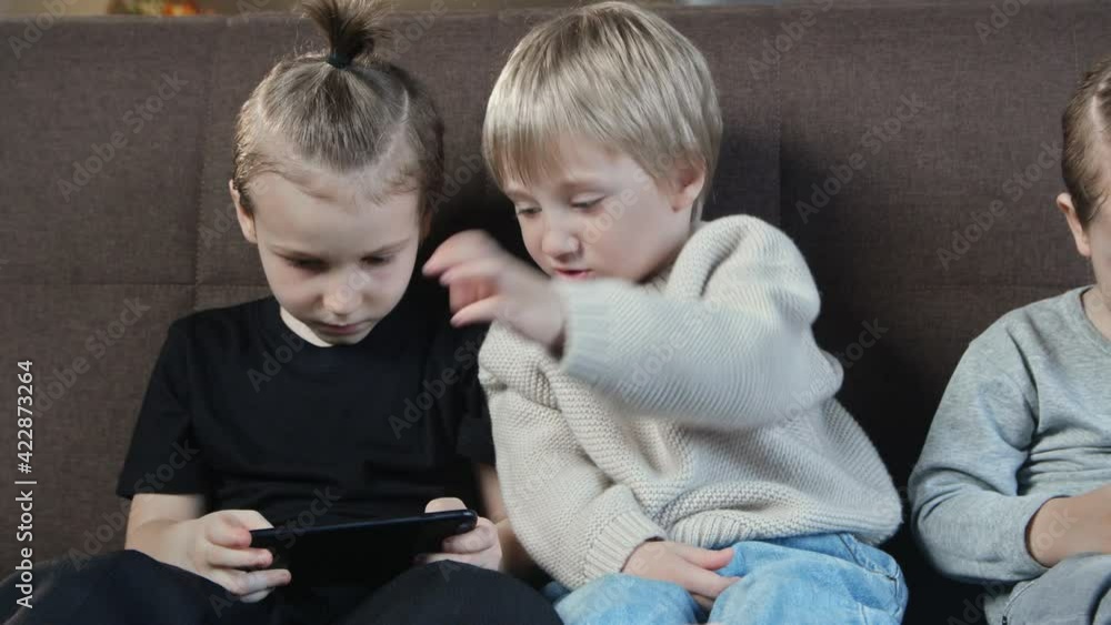 Close up of little smiling brothers playing the games on mobile phone at home. Close up of little smiling brothers playing the games on mobile phone at home.