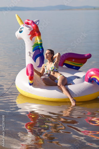 Girl swimming on white, trendy, blown up beach unicorn in summer in a pond