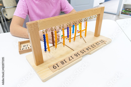 Girl in striped is playing and sorting a puzzle of colored plastic beads in montessori school.
