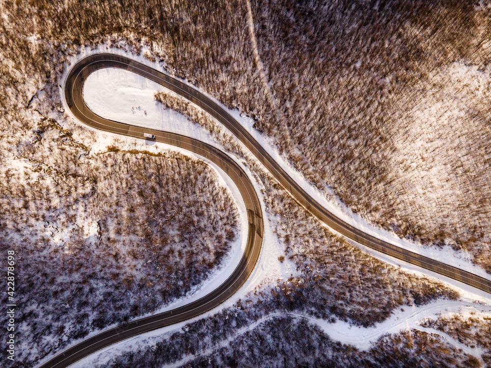 High angle aerial view drone image on the curved serpentine road trough the trees and forest in mountain range with white snow in winter day near Knjazevac in Serbia - Travel journey vacation concept