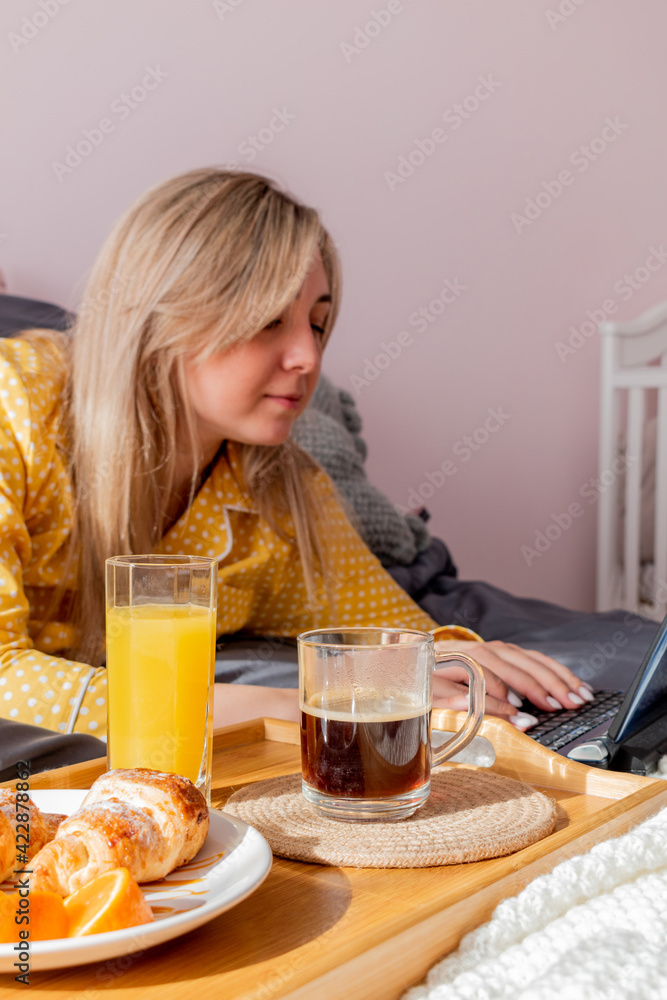 Young woman in yellow pajamas has healthy breakfast and work laptop while lying on bed in bedroom. Young woman in yellow pajamas has healthy breakfast and work laptop while lying on bed in bedroom.