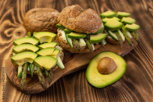Healthy vegetarian organic breakfast meal, sandwich food made from asparagus, avocado, cucumber, soft cheese on whole grain buns. Wooden board, close up