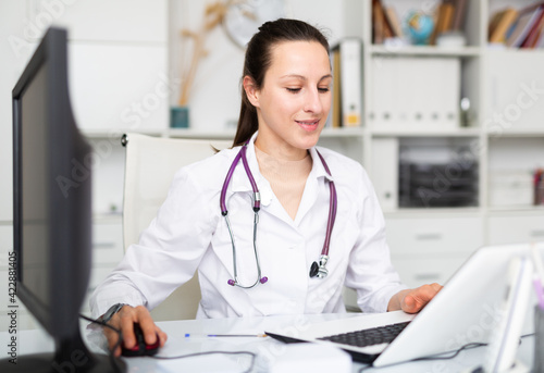 Woman doctor sitting at workplace with computer in her office