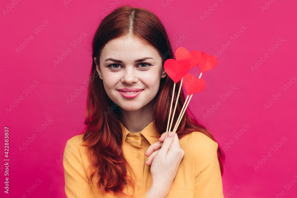 Fototapeta premium happy woman with red hearts on stick and yellow shirt pink background