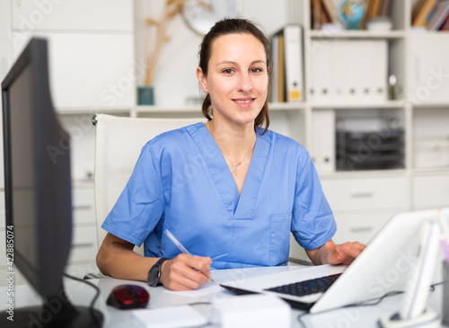 Portrait of female doctor who is working with laptop and documents in clinic
