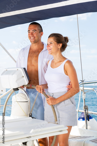 Young man and woman steering pleasure yacht, enjoying romantic sea travel on warm summer day © JackF