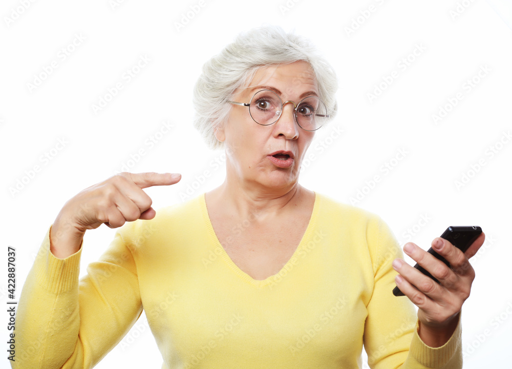 Exciting news. An elderly woman has heard the news and points to the phone with her finger, drawing attention. Exciting news. An elderly woman has heard the news and points to the phone with her finger, drawing attention.