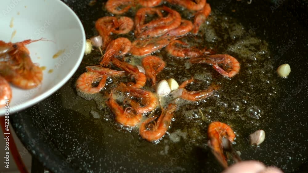 cook removing fried prawns from the heat and putting them on a plate during the preparation of fideua cook removing fried prawns from the heat and putting them on a plate during the preparation of fideua