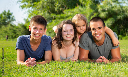 Happy parents with two kids laying on grass in sunny summer park. High quality photo