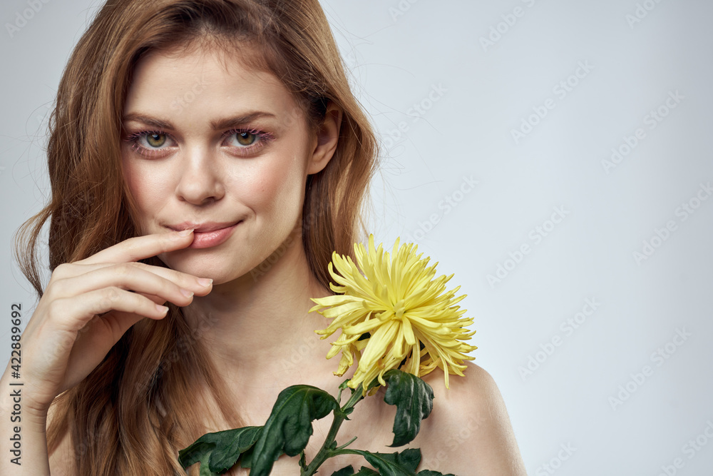Portrait of a beautiful woman with a yellow flower on a light background charming smile model red hair Portrait of a beautiful woman with a yellow flower on a light background charming smile model red hair
