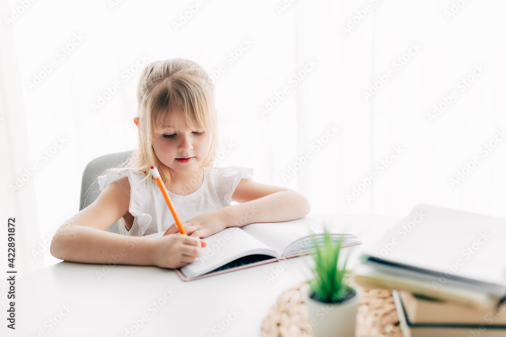 Girl writes in notebook at table. Education concept. Home schooling. Homework. Girl writes in notebook at table. Education concept. Home schooling. Homework.