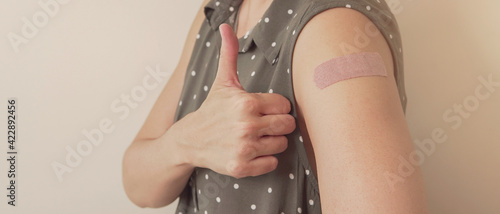 Foto woman showing thumb up and her arm with bandage after got vaccinated or  inocula