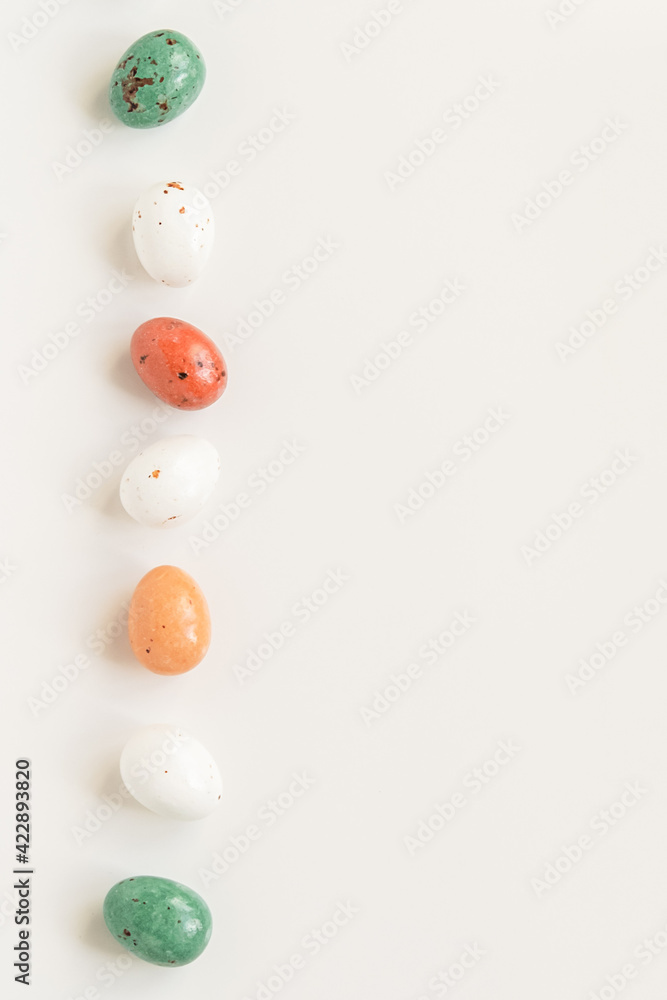 Easter minimal composition with multicolored eggs on the white background. Easter concept. Copy space, flat lay. Vertical photo.