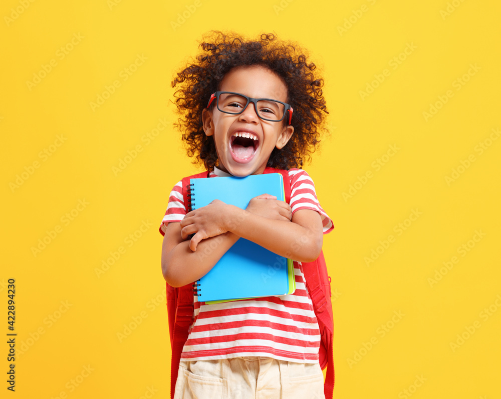 Cheerful little ethnic schoolchild with backpack and textbooks in yellow studio Cheerful little ethnic schoolchild with backpack and textbooks in yellow studio