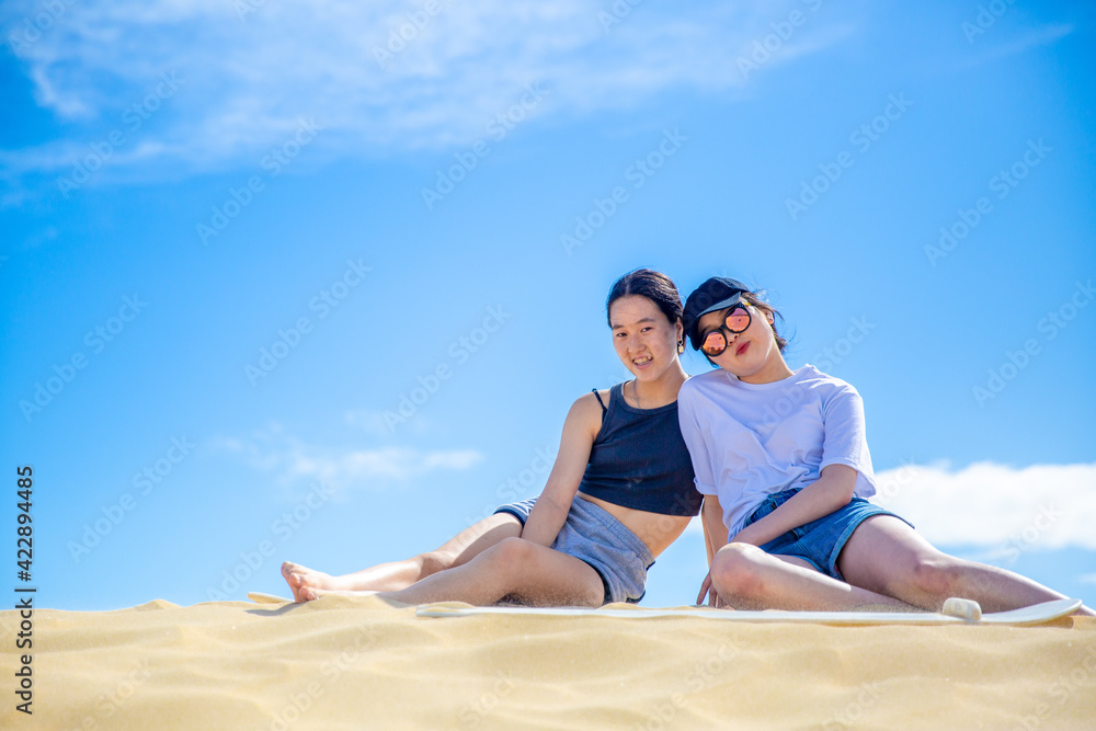 Two Chinese teenage girls leaning against each other in the sand dunes under sunny blue sky in holidays. Two Chinese teenage girls leaning against each other in the sand dunes under sunny blue sky in holidays.