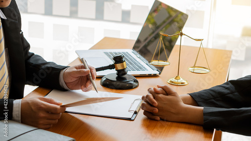 Φωτογραφία A lawyer advising clients at the desk in the office focuses on the hand with a hammer and scales on the desk with a laptop