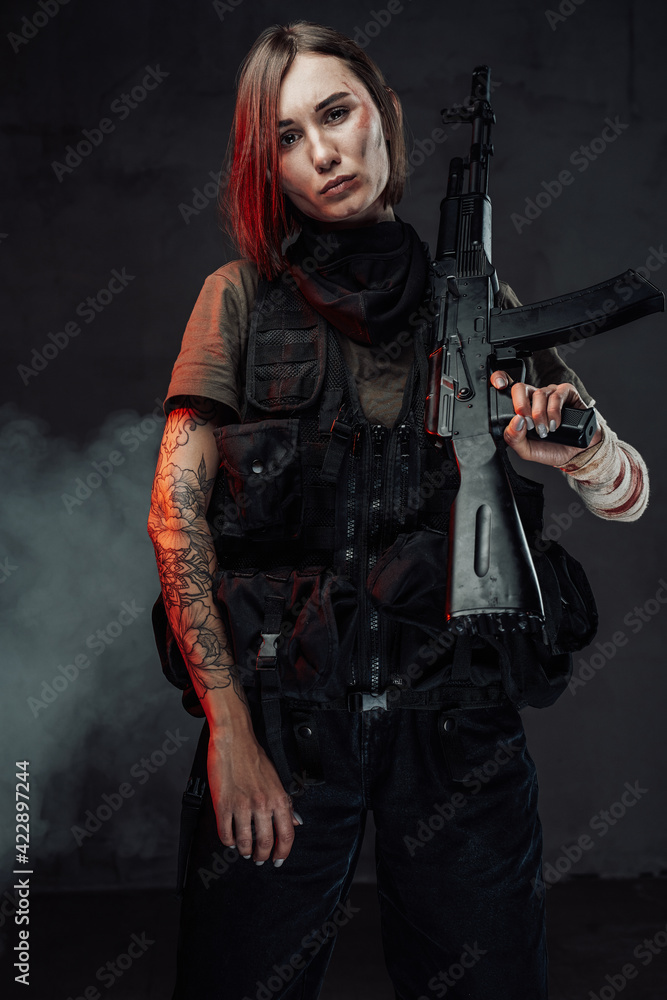 Fototapeta premium Beautiful female soldier with rifle on her shoulder in smokey background
