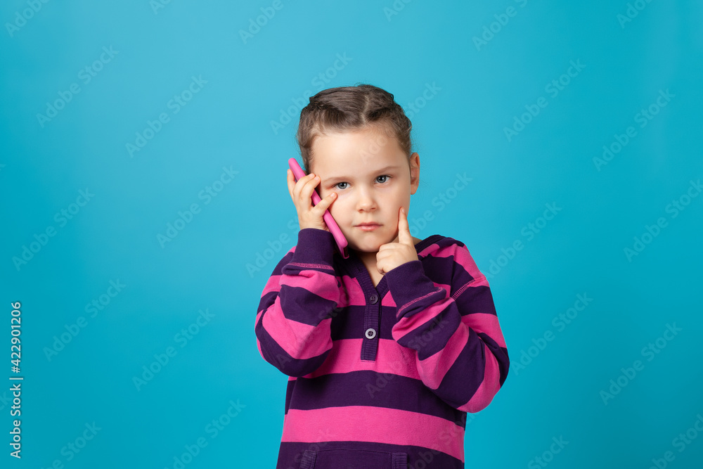 close-up portrait of a pensive, dreamy girl with pigtails talking on a mobile phone and holding a finger to her cheek, isolated on a blue background. close-up portrait of a pensive, dreamy girl with pigtails talking on a mobile phone and holding a finger to her cheek, isolated on a blue background.