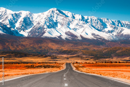 Beautiful road in autumn mountains. Chuysky tract and view of North-Chuya mountain ridge in Altai, Siberia, Russia. Snow-covered mountain peaks and yellow autumn forest