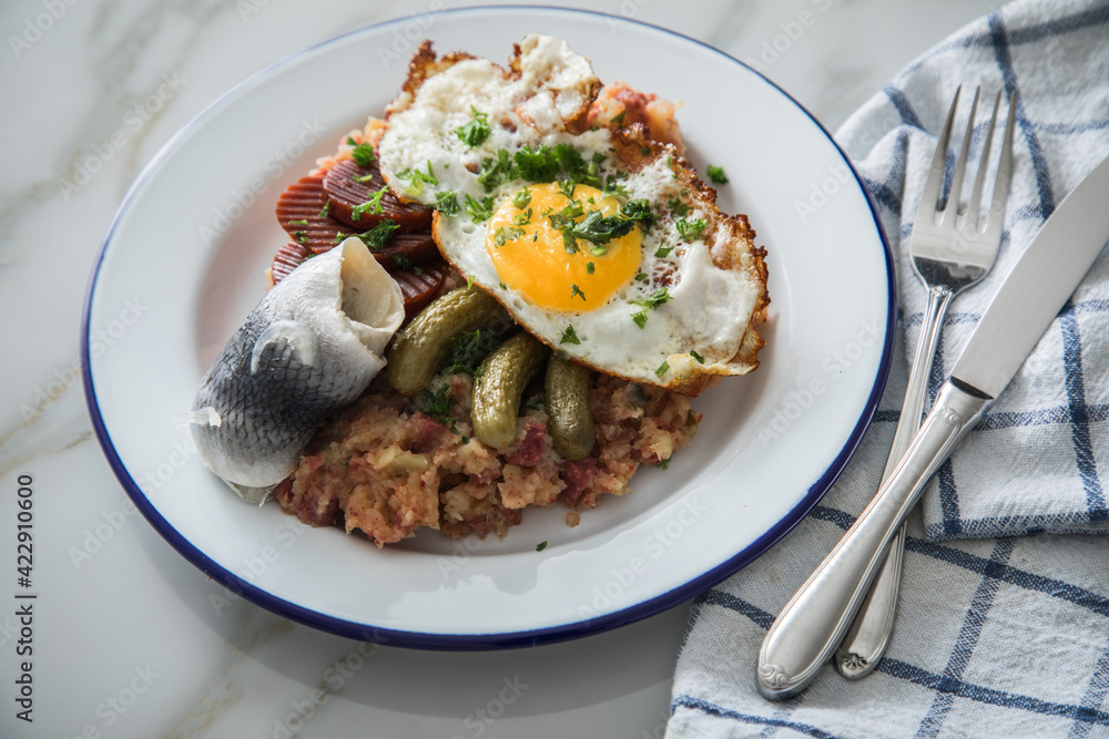 Norddeutscher Hamburger Labskaus mit Rindfleisch Corned Beef, Rote Beete, Kartoffeln, Saure Gurken, Spiegelei und Rollmops auf Emaille Teller