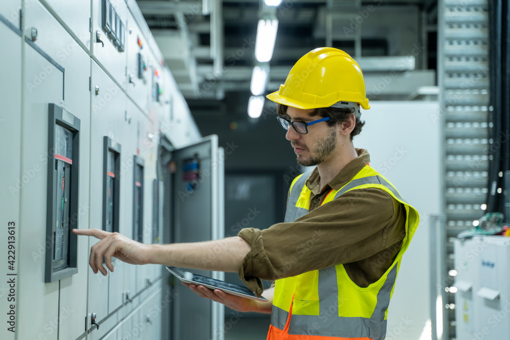 Portrait of electrician engineer use tablet computer taking notes at control room in factory.